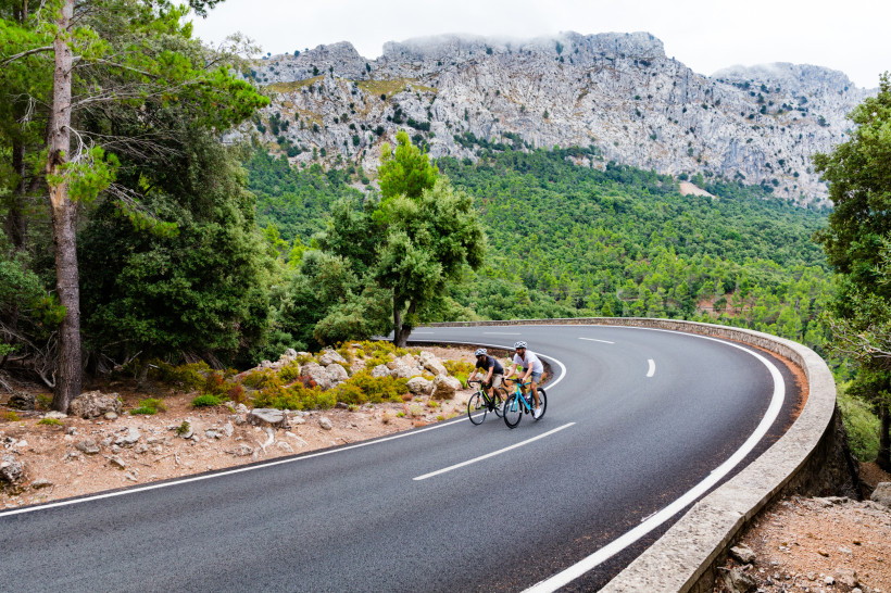 Rennradfahrer auf Bergstraße in der Gemeinde Calvia Zwei Rennradfahrer auf kurviger Bergstraße in der grünen Hügellandschaft von Calvia auf Mallorca