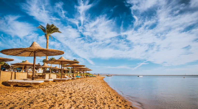 Ruhiger Sandstrand mit Strohliegen und Palmen unter blauem Himmel am klaren Meer