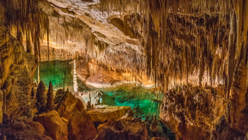 Drachenhöhlen, Mallorca Beleuchtete Tropfsteinhöhle mit Stalaktiten und Stalagmiten sowie einem türkisfarbenen unterirdischen See in den Drachenhöhlen auf Mallorca