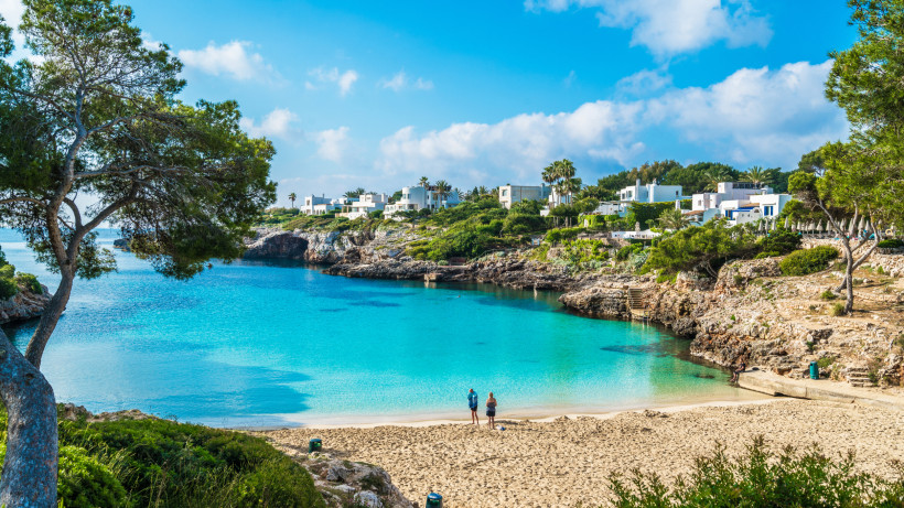 Kleine Badebucht in Cala d’Or mit weißen Häusern im Ibiza-Stil, Pinien und klarem Wasser in entspannter Atmosphäre