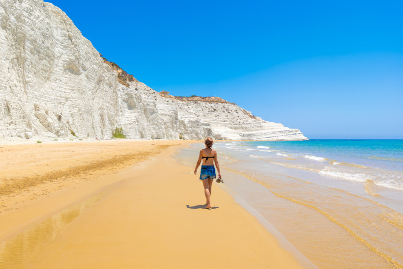 Scala dei Turchi – strahlend weiße Klippen an Siziliens Südküste Frau spaziert am goldenen Sandstrand unter den weißen Kalksteinfelsen der Scala dei Turchi nahe Realmonte auf Sizilien – beeindruckendes Naturwunder am Mittelmeer