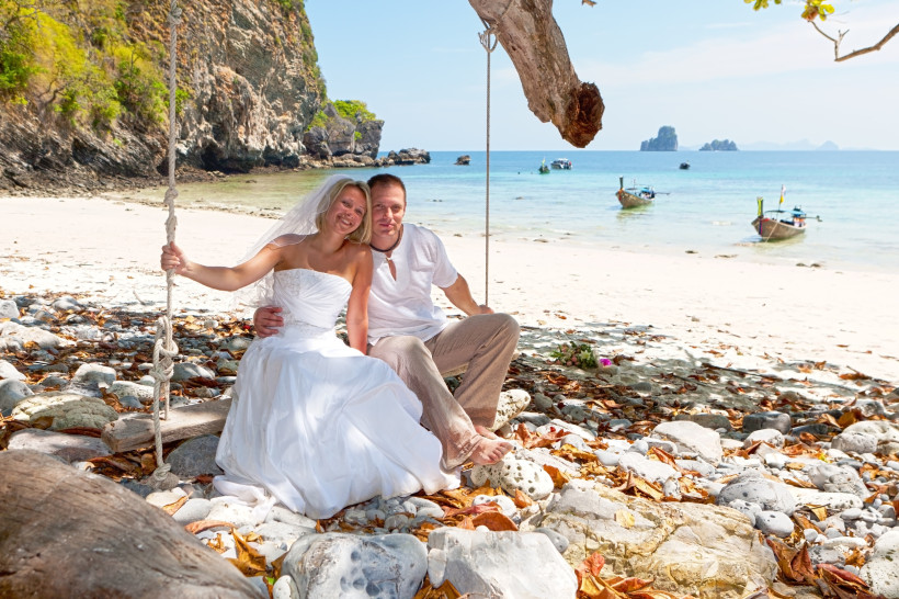 Hochzeitspaar am Strand in Thailand – Romantische Hochzeitsreise im Tropenparadies Frisch verheiratetes Paar sitzt am Strand in Thailand auf einer Schaukel mit Blick aufs Meer – romantische Hochzeitsreise und Honeymoon im tropischen Paradies.