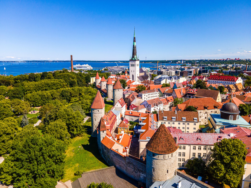 Blick auf die Altstadt von Tallinn mit Stadtmauer und Türmen, roten Dächern und Kirchturm am Hafen