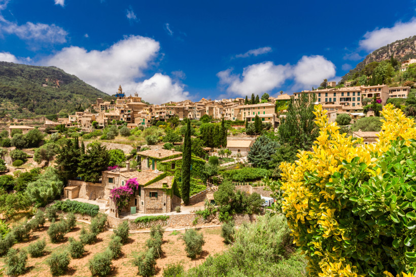 Blick auf Valldemossa in der Serra de Tramuntana mit Natursteinhäusern, Olivenhainen und Bergen unter blauem Himmel
