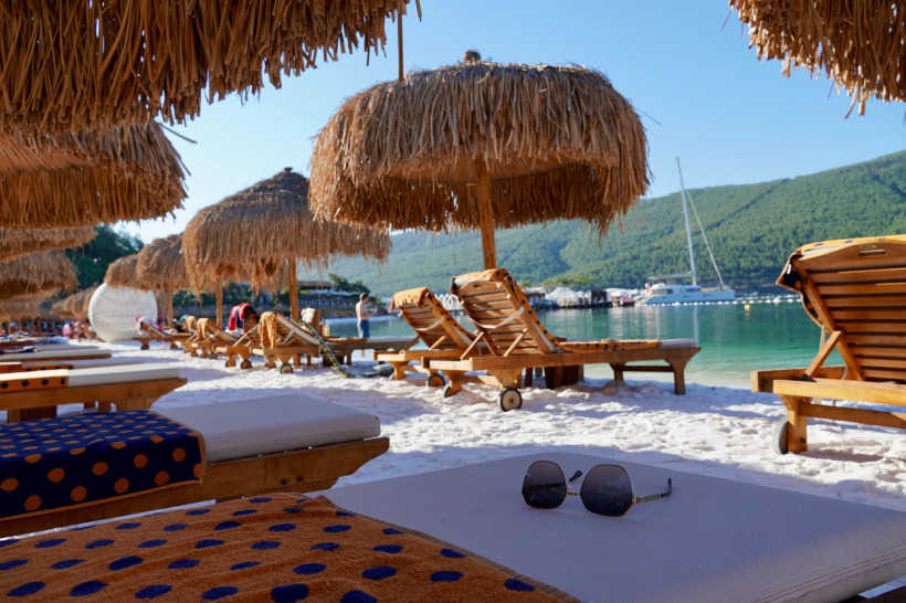 Liegestühle und Strohs Sonnenschirme am Strand von Bodrum mit türkisfarbenem Meer und grünen Hügeln im Hintergrund