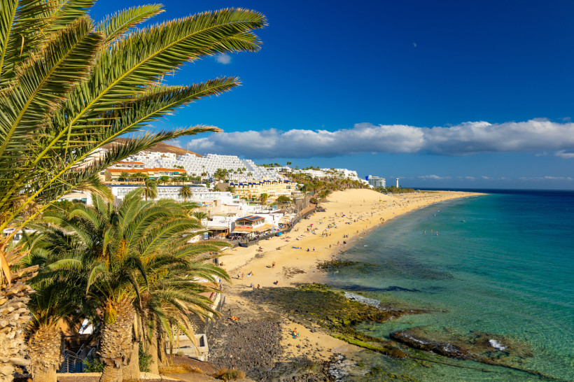 Blick auf Morro Jable und die Playa del Matorral mit Palmen im Vordergrund, Sandstrand, Hotelanlagen und türkisfarbenem Meer
