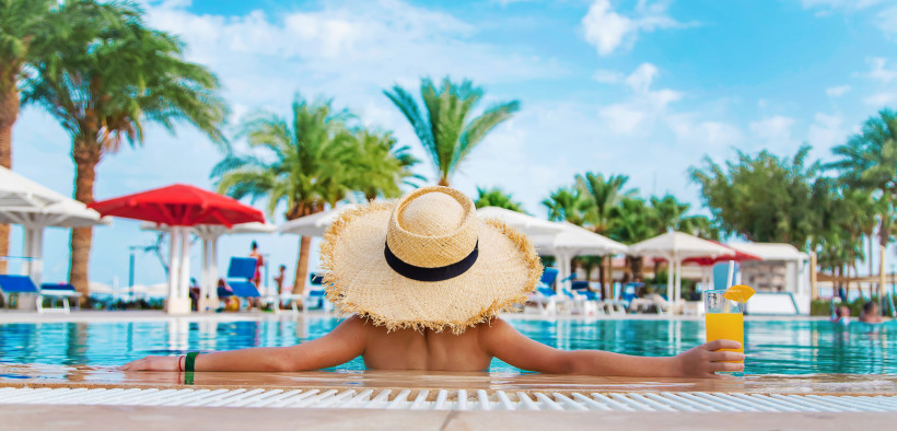 Urlauber mit Strohhut entspannt im Pool unter Palmen während eines All-Inclusive-Urlaubs auf Lanzarote.