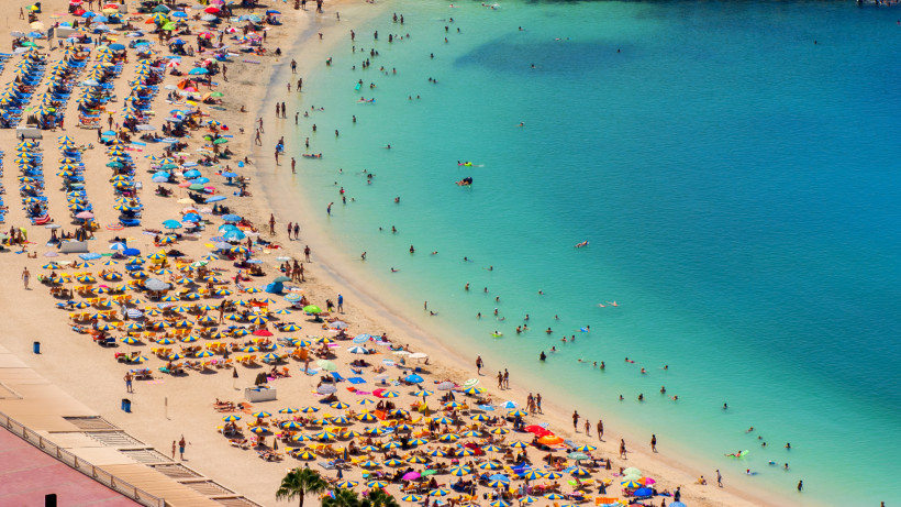Blick auf die Playa de Amadores auf Gran Canaria mit vielen Sonnenschirmen am Sandstrand und Badenden im türkisfarbenen Meer