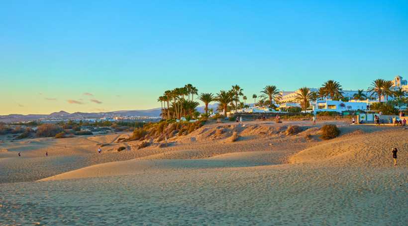 Sanddünen von Maspalomas mit Palmen und Gebäuden im Hintergrund