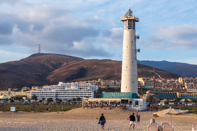 Leuchtturm Faro de Morro Jable am Strand, im Hintergrund Hügel und Hotels