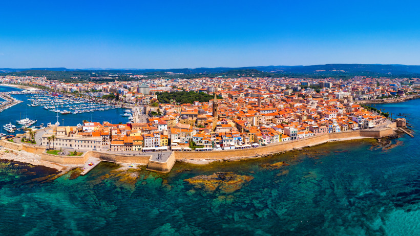Panoramablick auf Alghero auf Sardinien mit Altstadt, Stadtmauer und Hafen im türkisblauen Mittelmeer – Sehenswürdigkeit an der Nordwestküste der Insel