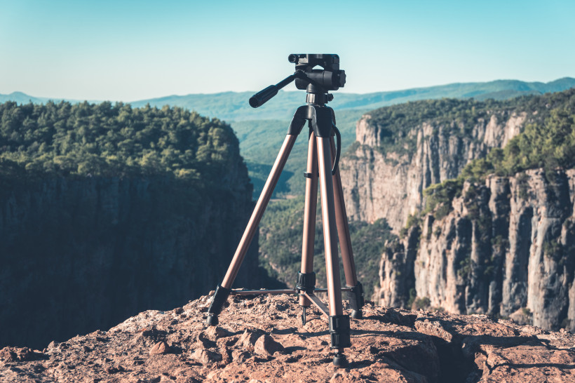Ein Kamerastativ steht auf einem felsigen Aussichtspunkt mit Blick auf eine tiefe Schlucht und bewaldete Berge im Hintergrund.