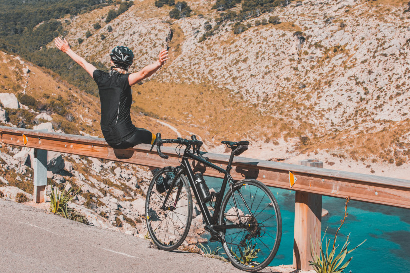 Radfahrerin mit Rennrad auf Küstenstraße nahe Calas de Mallorca mit Blick auf die türkisfarbene Steilküste