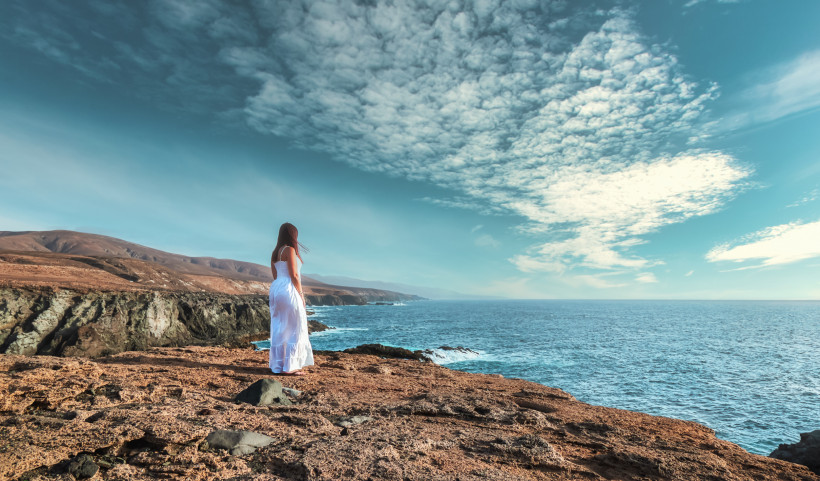 Frau auf Klippe mit Blick auf die Westküste von Fuerteventura und den Atlantik