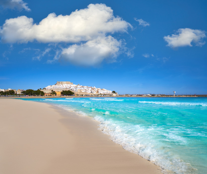 Strand mit türkisfarbenem Meer und Blick auf die Altstadt und Burg von Peñíscola, Spanien