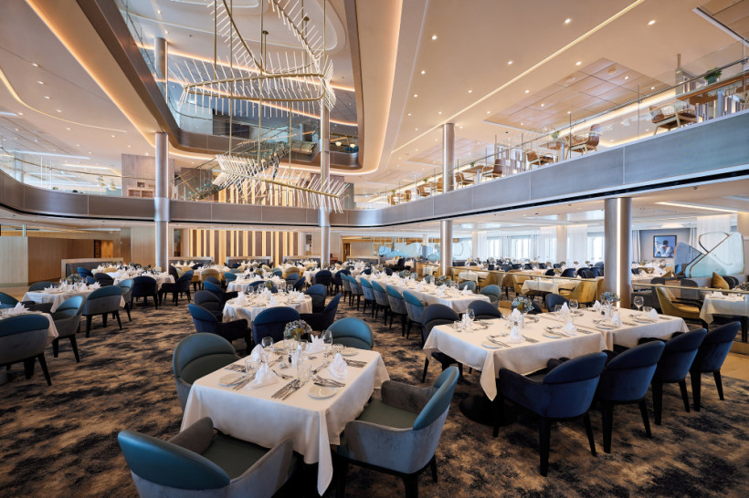 Hauptrestaurant an Bord der Mein Schiff 7 mit gedeckten Tischen, Sitzgruppen und mehrstöckigem Innenraum mit großem Kronleuchter