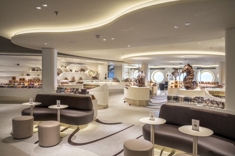 MSC World Europa – Jean-Philippe Chocolat & Café, Innenansicht Innenbereich des Jean-Philippe Chocolat & Café an Bord der MSC World Europa mit Sitzbereich, Verkaufstheken und Schokoladenskulpturen