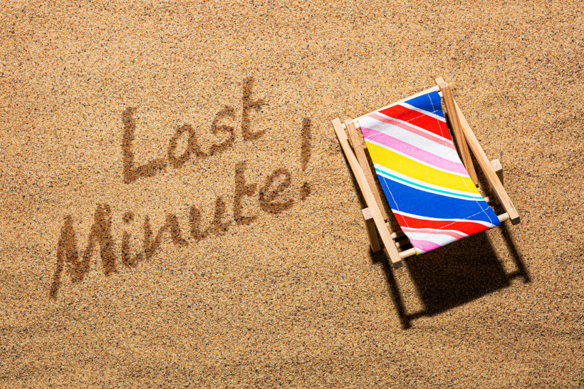 Bunter Liegestuhl am Strand mit der Aufschrift Last Minute im Sand