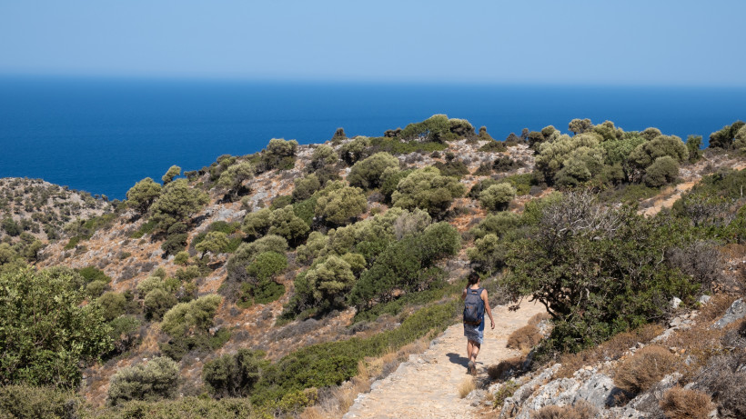 Wanderweg auf Kreta mit Blick auf das Meer und eine Person mit Rucksack
