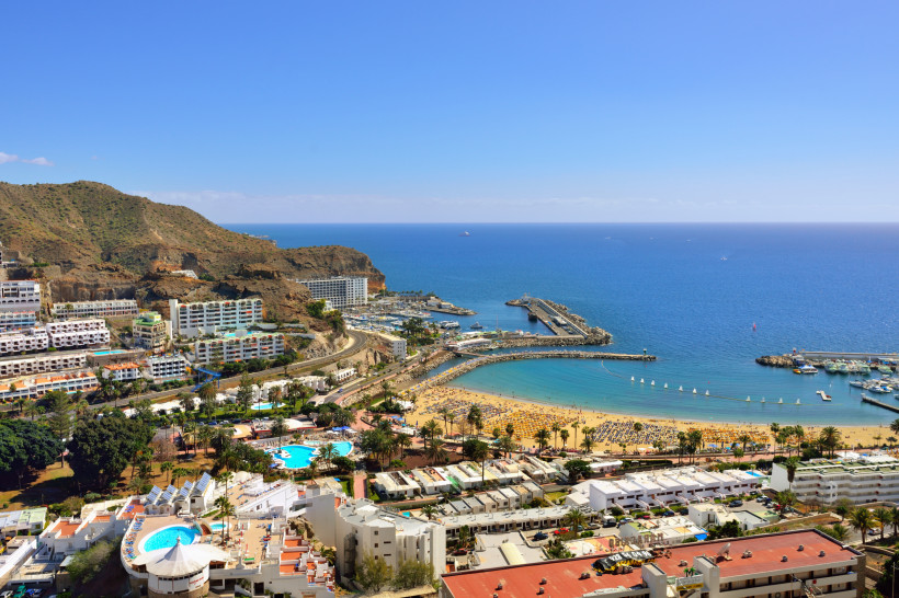 Blick über Puerto Rico auf Gran Canaria mit Strand, Hafenmole und Hotels an der Küste