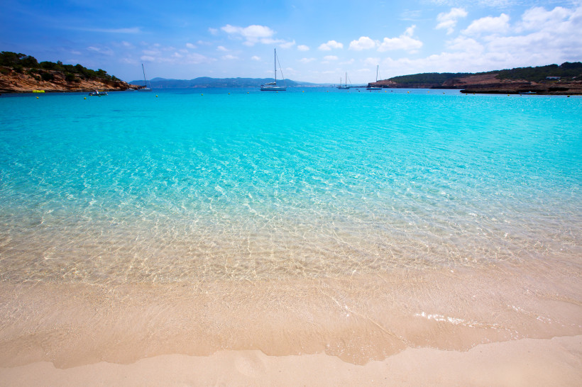 Cala Bassa mit türkisfarbenem Meer, Sandstrand und Segelbooten in der Bucht