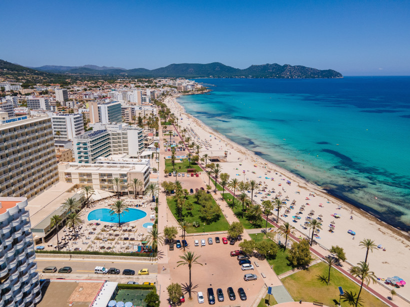 Luftaufnahme von Cala Millor mit langem Sandstrand, türkisblauem Meer, Palmenpromenade und Hotels direkt an der Küste auf Mallorca.