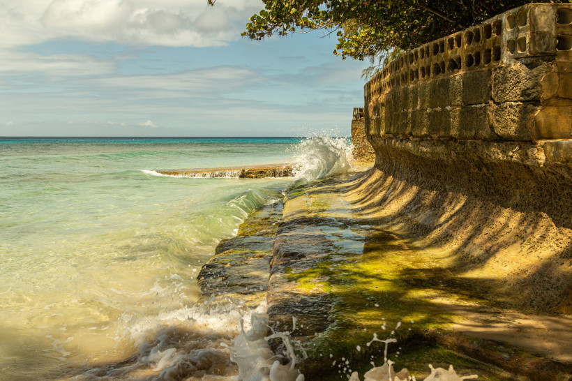 Karibisches Meer mit türkisblauem Wasser, das gegen eine alte Ufermauer auf Barbados schlägt.