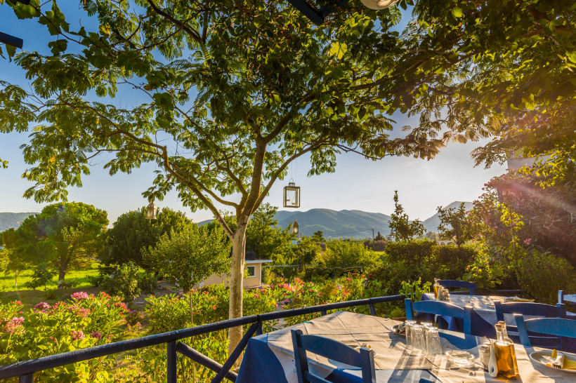Taverna in einem Bergdorf bei Chersonissos mit Tisch für zwei und Blick auf die Berge Taverna-Terrasse in einem Bergdorf bei Chersonissos mit gedecktem Tisch für zwei, Baum und Blick auf die Berge