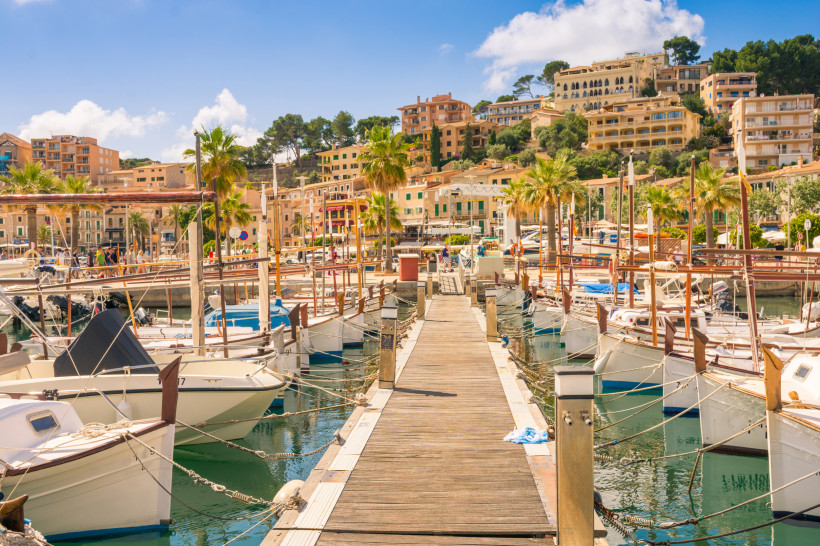 Hafen von Port de Sóller mit Steg, festgemachten Booten, Palmen und Promenade vor Hangbebauung