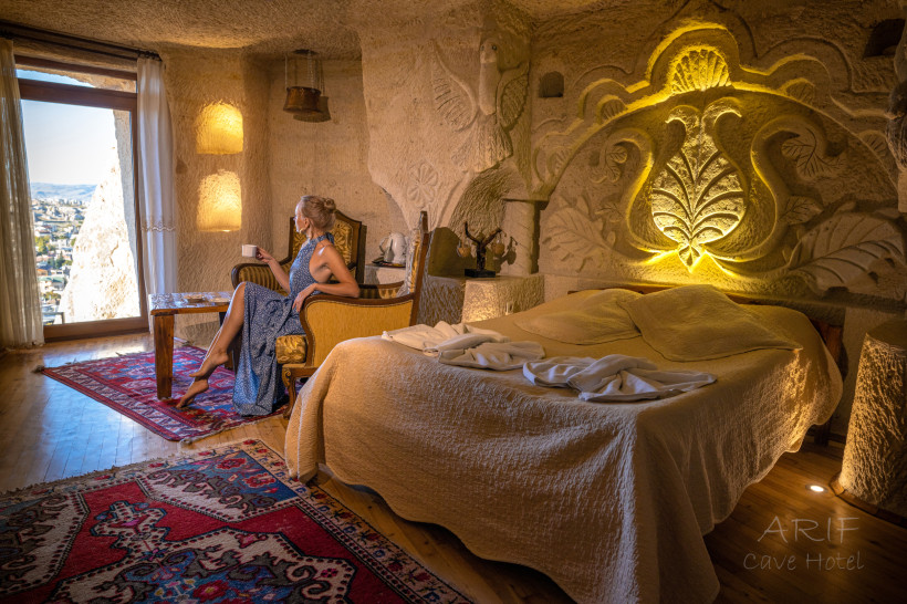 Türkei Frau sitzt mit einer Tasse in einem luxuriösen Höhlenhotelzimmer mit kunstvollen Steinverzierungen und Blick auf die Landschaft
