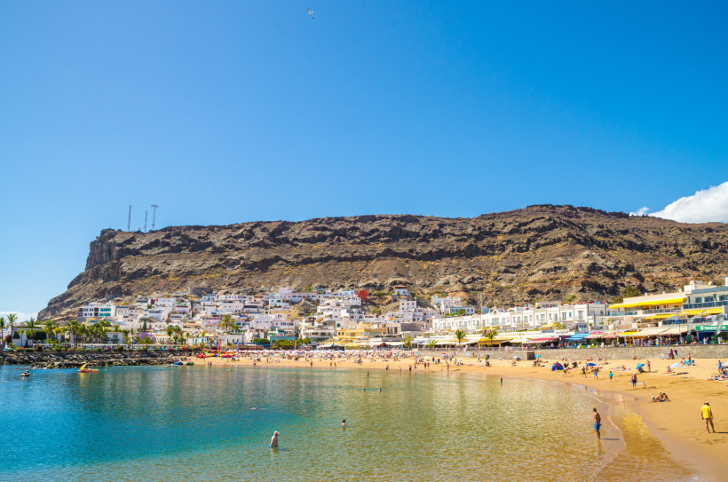 Playa de Mogán, Puerto de Mogán Strand Playa de Mogán in Puerto de Mogán mit Badegästen, Promenade und Felsmassiv im Hintergrund