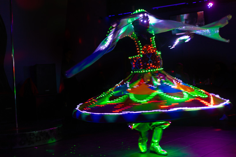 Ägypten - Sharm el Sheikh Ein Tanoura-Tänzer führt einen traditionellen ägyptischen Derwisch-Tanz auf. Er trägt ein farbenfrohes, weit ausgestelltes Kostüm, das mit leuchtenden LED-Lichtern geschmückt ist. Die Lichter erzeugen während der Drehung kreisförmige Muster. Die Szene ist