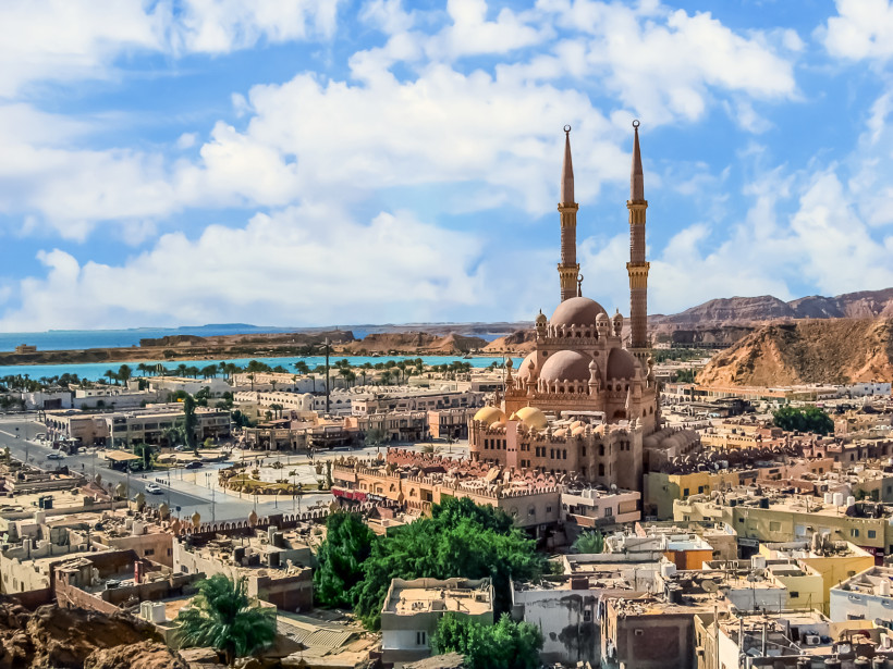 Ägypten - Sharm el Sheikh Panoramablick über die Stadt Sharm el Sheikh in Ägypten mit der imposanten Al Sahaba Moschee im Zentrum. Die Moschee hat zwei hohe Minarette und mehrere goldene Kuppeln. Sie ist von flachen Gebäuden, Straßen und grünen Palmen umgeben. Im Hintergrund sieht