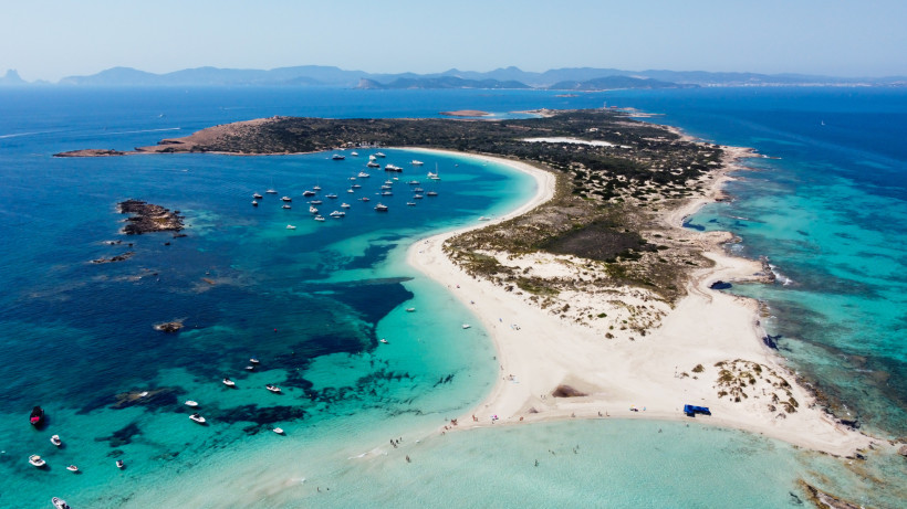 Luftaufnahme einer sandigen Landzunge mit türkisfarbenen Buchten und ankerten Booten vor Formentera