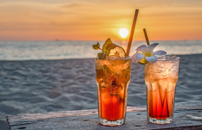 Zwei erfrischende Cocktails mit Minze und Zitrone auf einem Holztisch am Strand bei Sonnenuntergang
