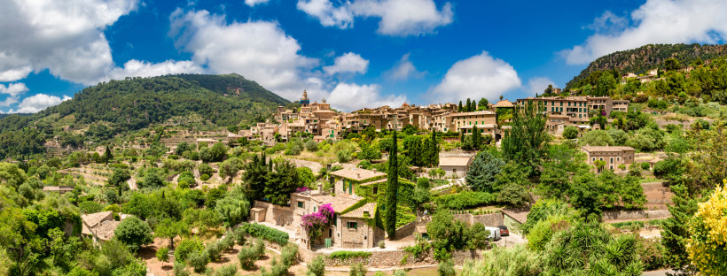 Valldemossa: Ortsansicht mit Häusern am Berghang und mediterraner Vegetation Blick auf Valldemossa mit Natursteinhäusern am Hang, Zypressen und grüner Vegetation unter blauem Himmel