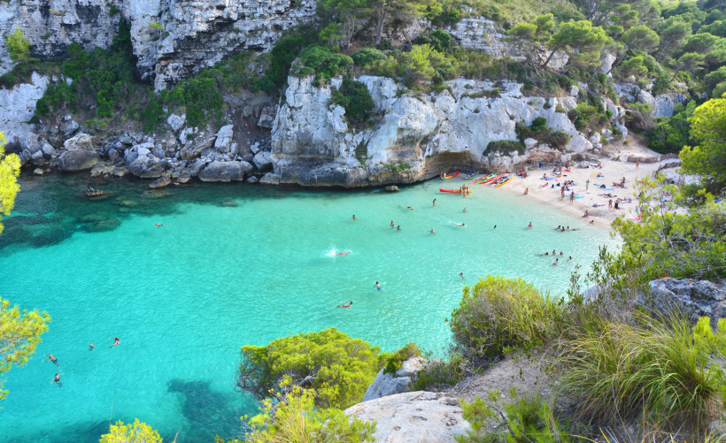 Cala Macarella auf Menorca: idyllische Bucht mit feinem Sandstrand, türkisblauem Wasser und umgeben von steilen Felsen und Pinienwäldern.
