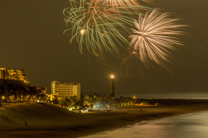 Fuerteventura Feuerwerk über einem nächtlich beleuchteten Strand mit Leuchtturm und Hotels im Hintergrund.