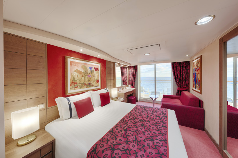 Schlafbereich einer Deluxe Balcony Aurea Kabine auf der MSC Orchestra mit Doppelbett, Sofa und Balkonblick aufs Meer
