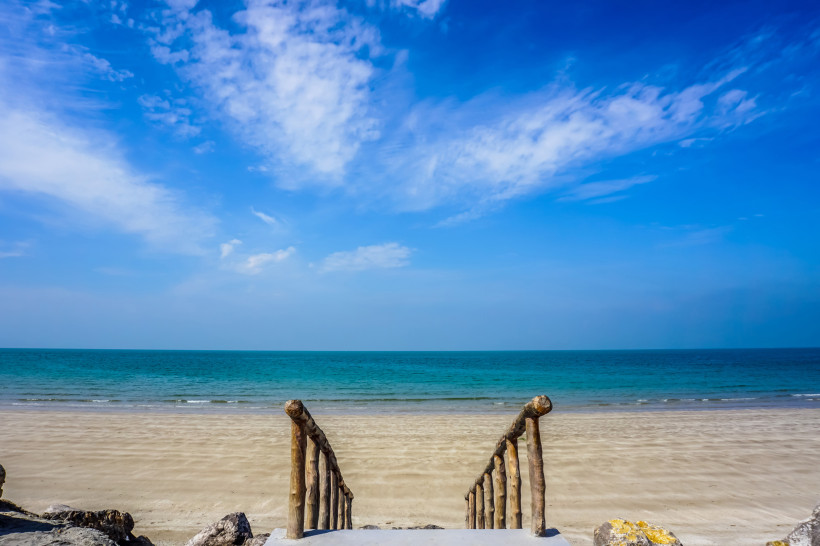 Ras al-Khaimah, Strandurlaub Holztreppe führt zu einem ruhigen Sandstrand mit türkisblauem Meer und klarem Himmel