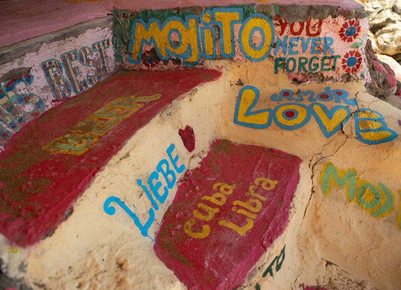 Kreta Eine bemalte Steintreppe mit bunten Worten und Schriftzügen wie 'LOVE', 'MOJITO', 'Cuba Libra', 'LIEBE' und weiteren in verschiedenen Sprachen. Die Farben sind kräftig und lebendig – Rot, Gelb, Blau – und vermitteln ein künstlerisches, freies Flair. Die O