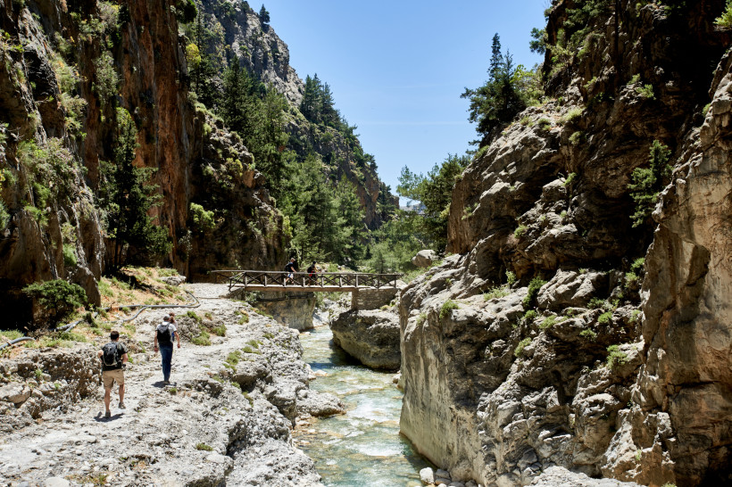 Wanderweg in der Samaria-Schlucht mit Felswänden, Bachlauf und kleiner Holzbrücke