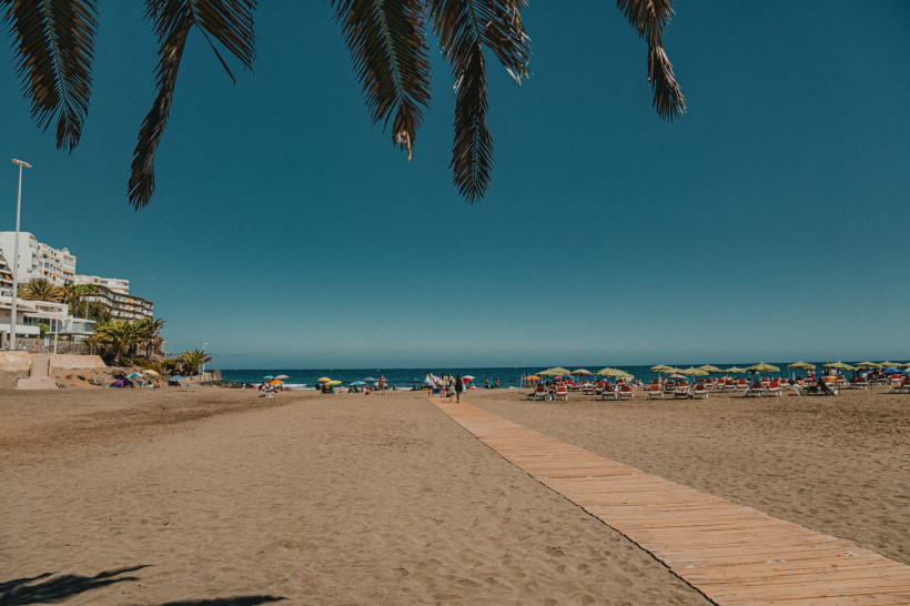Strand von San Agustín auf Gran Canaria mit Holzsteg, Liegen und Sonnenschirmen am Meer