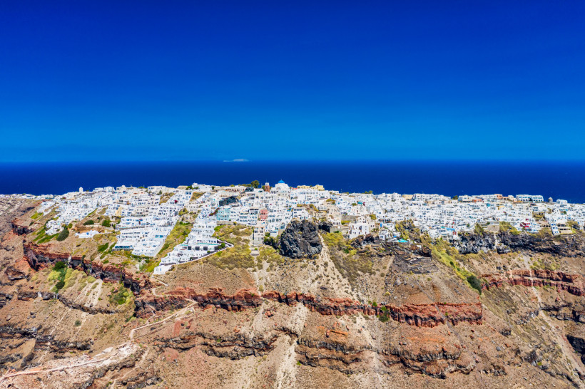 Santorini - Imerovigli  Imerovigli auf Santorini aus der Luft: weiße Häuser auf der Kraterkante, rote Lavaschichten und der Skaros-Felsen vor tiefblauer Ägäis
