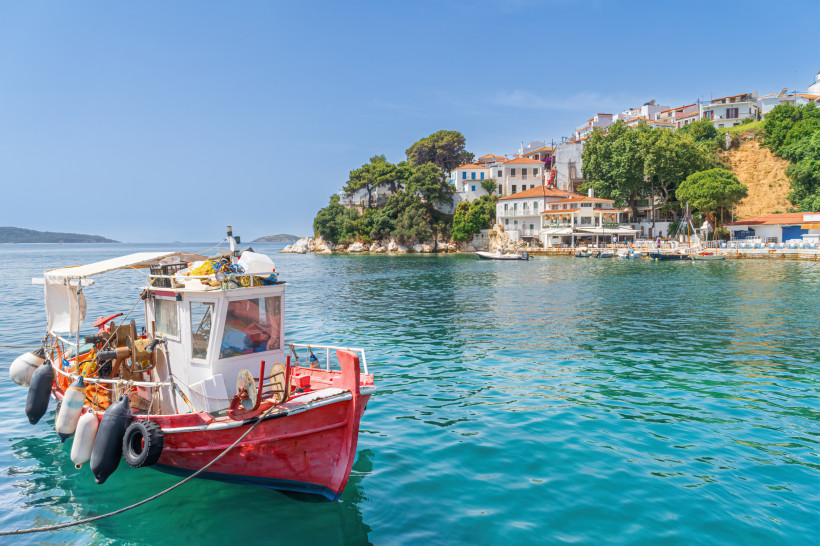 Rotes Fischerboot im Hafen vor der Küste von Skiathos mit Häusern am Hang