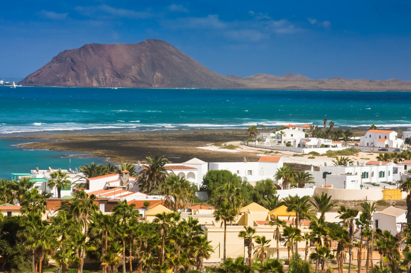 Blick auf Corralejo mit weißen Häusern und Palmen, dahinter türkisfarbenes Meer und Insel Lanzarote am Horizont