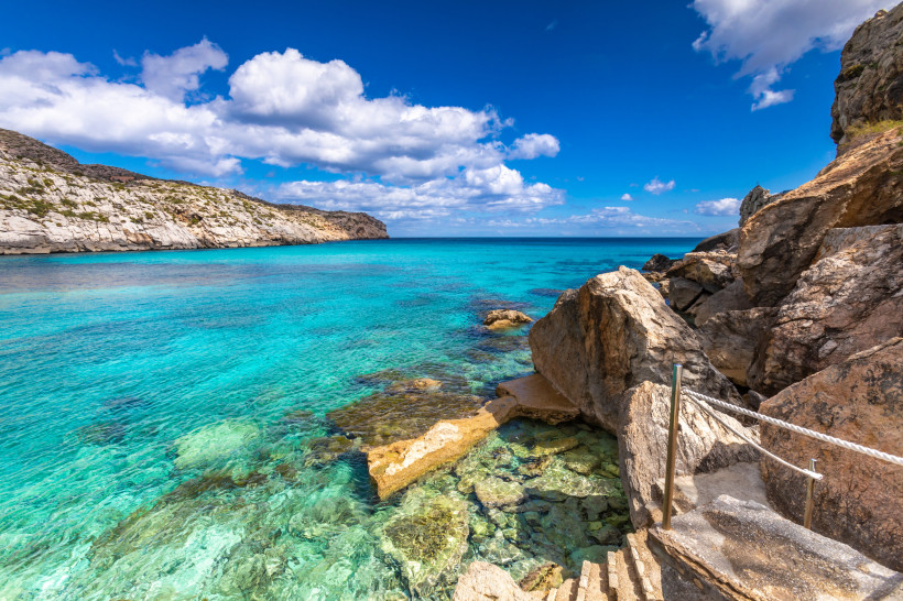 Felsige Küste an der Cala Clara mit türkisblauem, klarem Meer und Steintreppe am Ufer