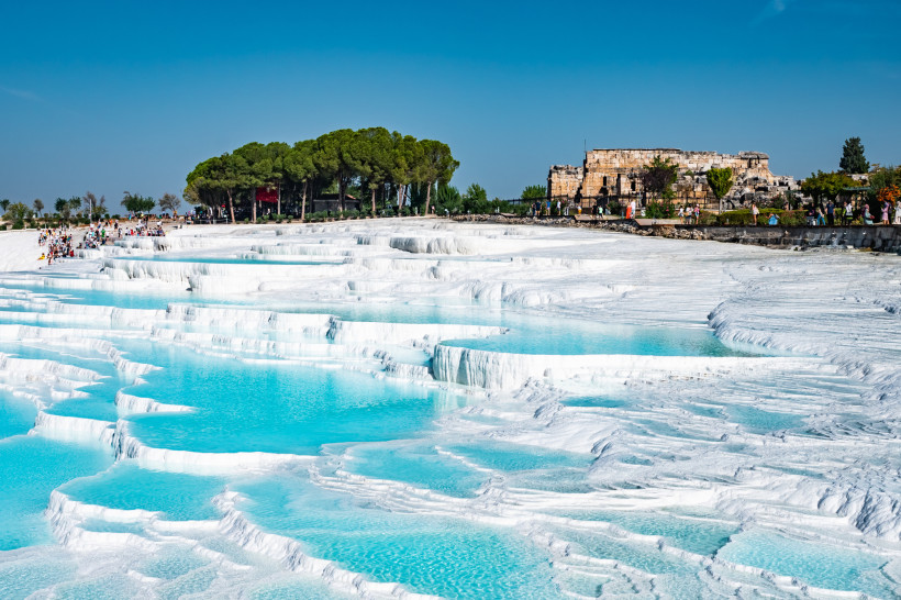Türkei - Pamukkale Pamukkale in der Türkei mit schneeweißen Kalksinterterrassen und türkisblauem Thermalwasser, im Hintergrund römische Ruinen