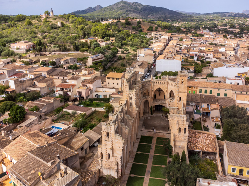 Luftaufnahme der unvollendeten Kirche Església Nova im Zentrum von Son Servera auf Mallorca, umgeben von Natursteinhäusern und engen Gassen im historischen Ortskern.