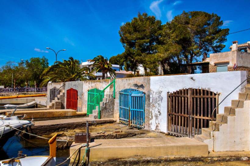 Barracas am Hafen von Portocolom im Viertel Cas Antic mit farbigen Holztoren und Booten am Kai